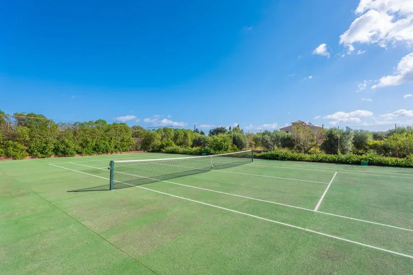 An outdoor tennis court with a net and green fencing.