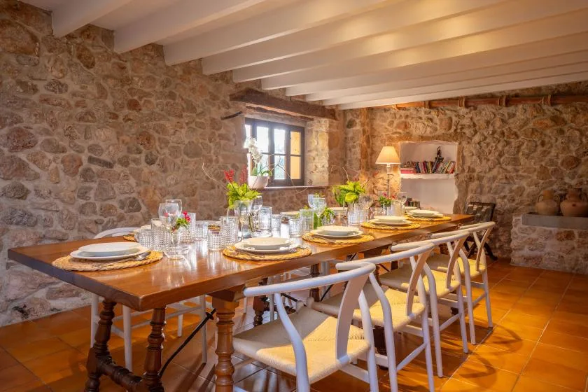 A dining room with a long wooden table set with dishes and chairs.