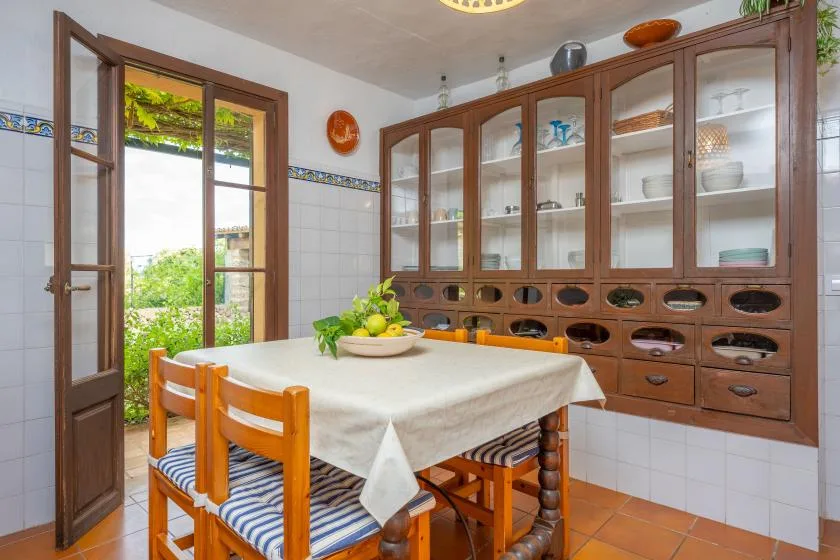 A tiled dining room with a wooden table and chairs beside tall glass-front cabinets.