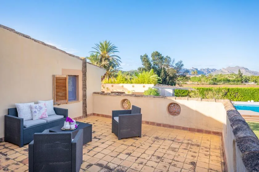 A tiled outdoor terrace has cushioned seating, a low wall, and views of the surrounding landscape.