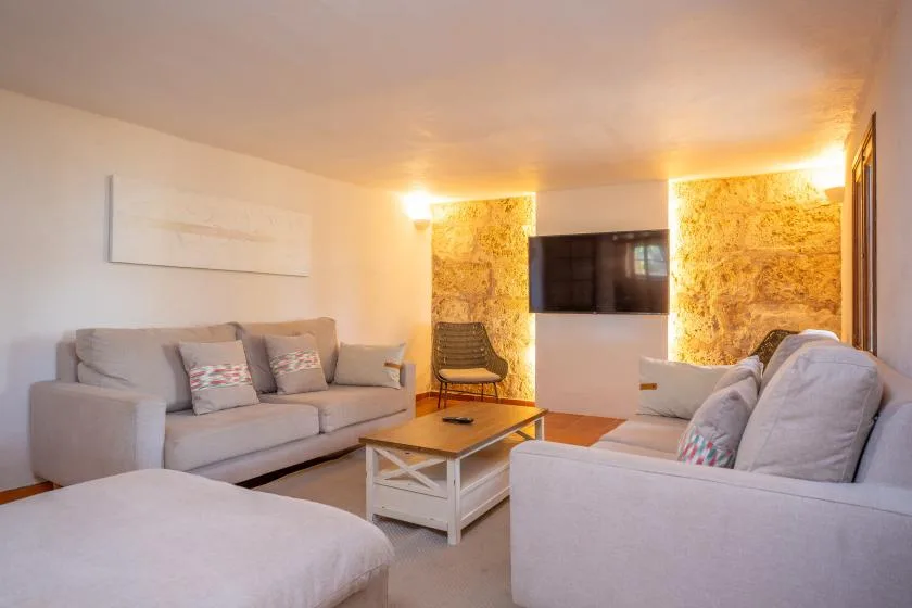 A living room with seating around a coffee table and a wall-mounted television.