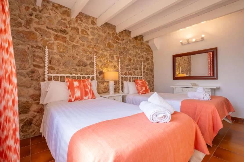 A bedroom with two beds, orange bedding, and an exposed stone wall.
