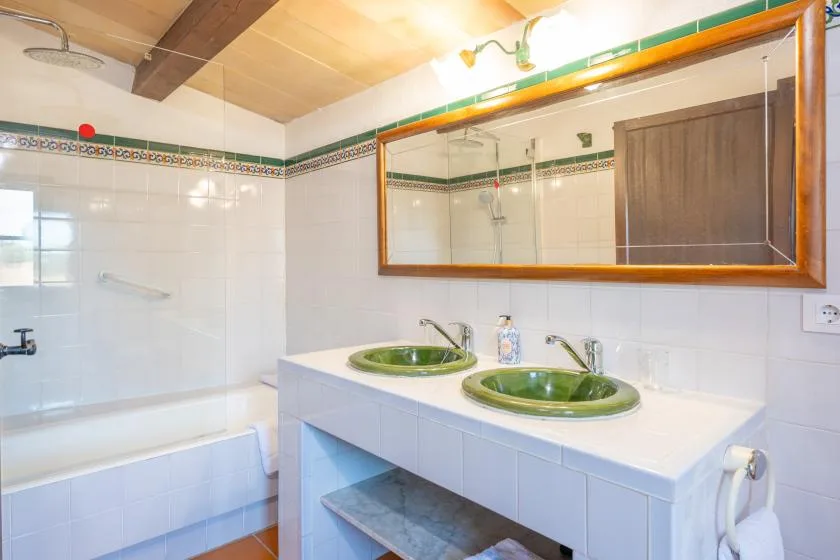 A tiled bathroom with a bathtub, two green sinks, and a large wall mirror.