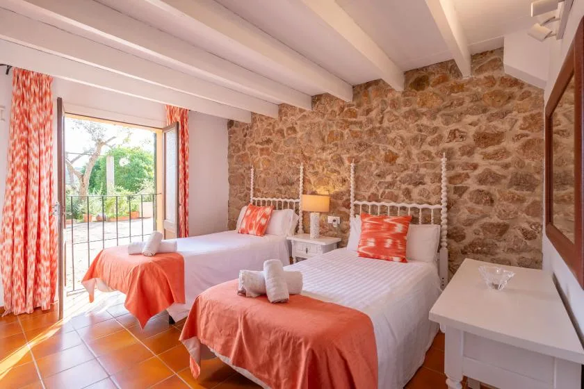 A bedroom with two beds, coral-colored bedding, and a stone wall.