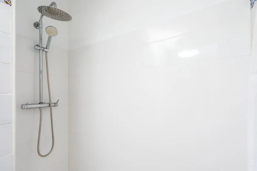 A tiled shower area with a wall-mounted showerhead and handheld sprayer.