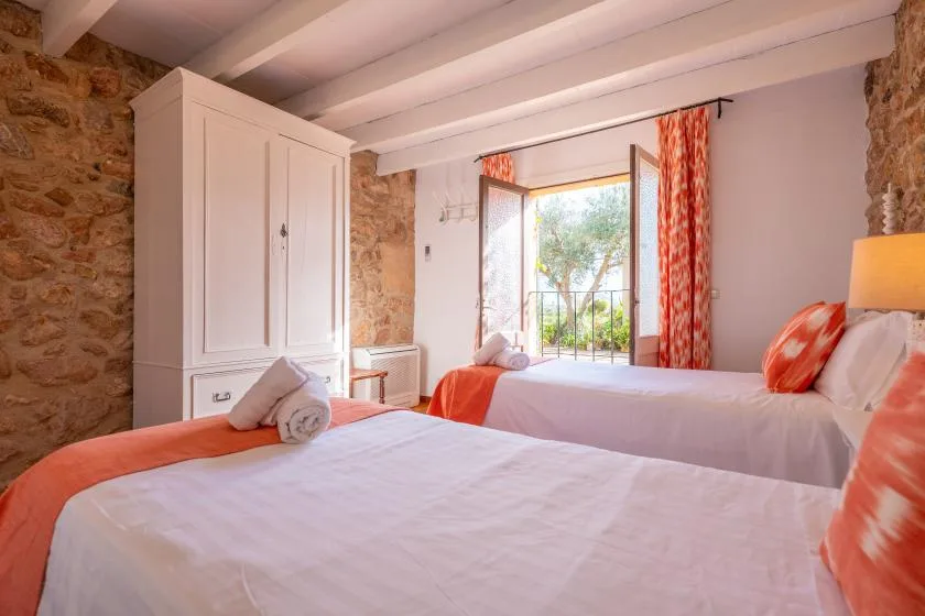 A bedroom with two beds and an open window overlooking greenery.