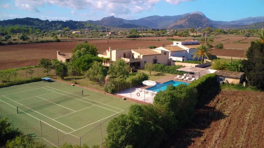 A rural property with a tennis court and swimming pool sits among fields.