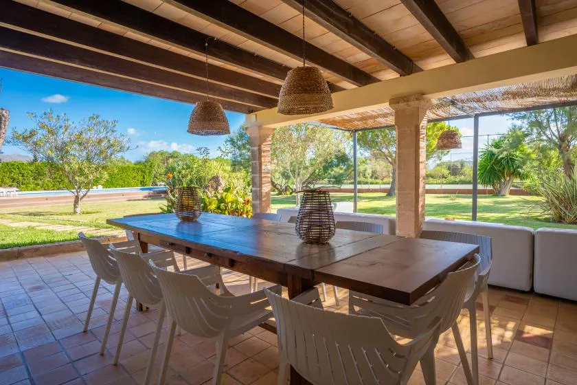 A covered outdoor dining area with a long table and garden views.