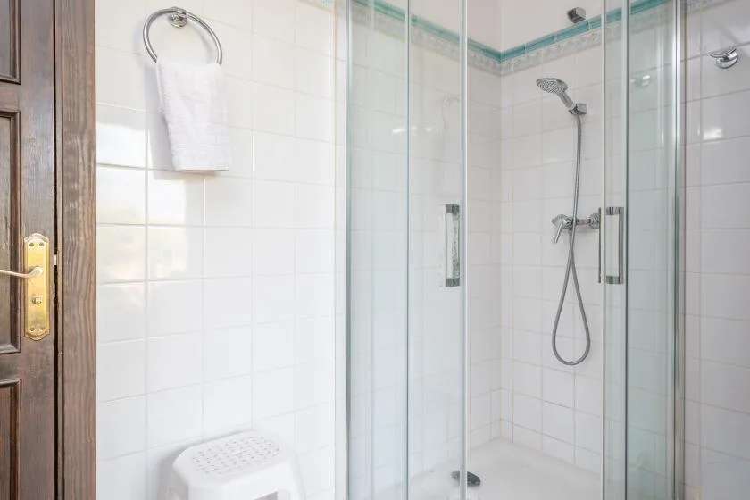 A tiled bathroom with a glass shower and a towel hanging on the wall.