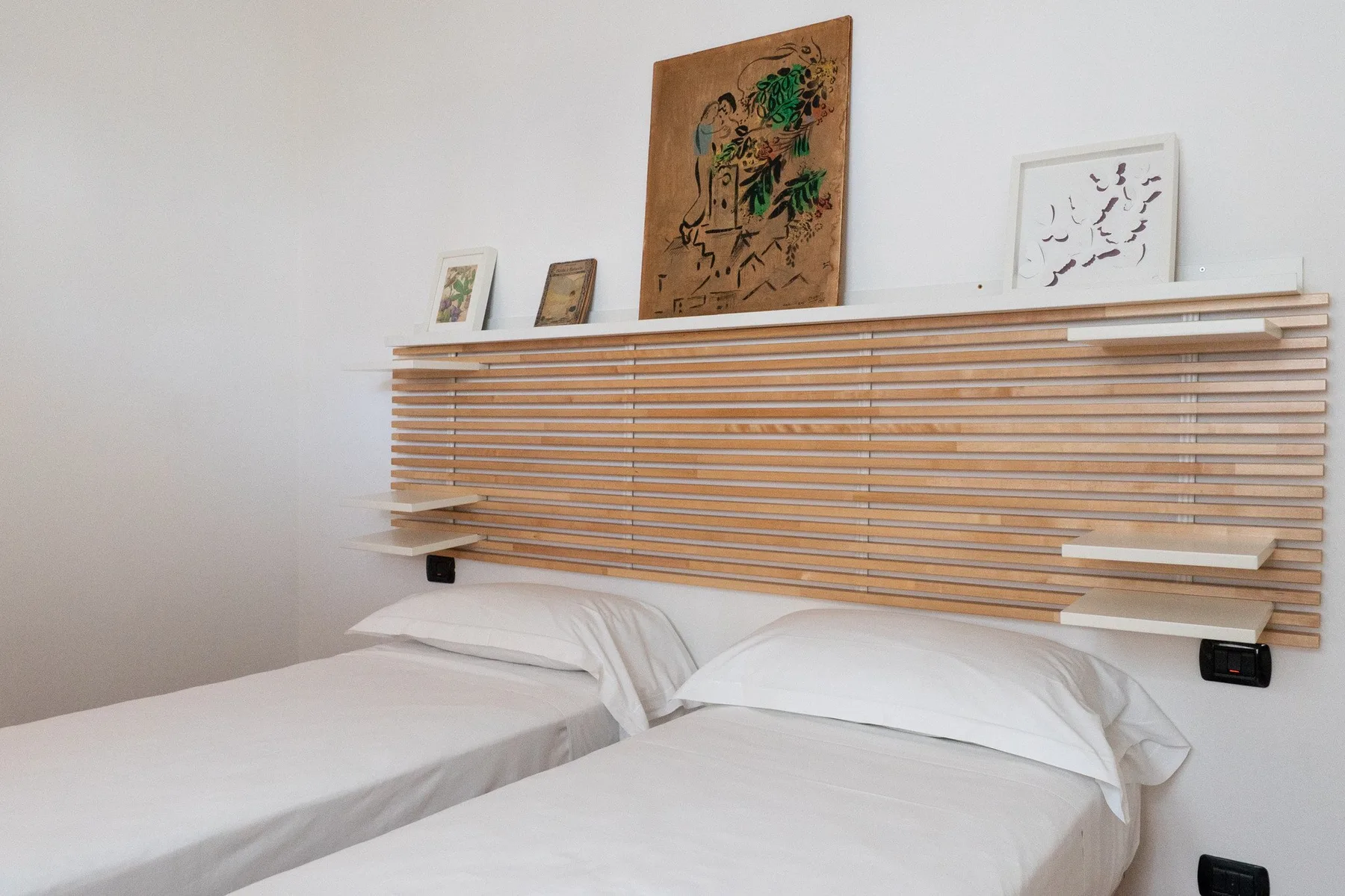 Un dormitorio con dos camas bajo un cabecero de listones de madera y cuadros.