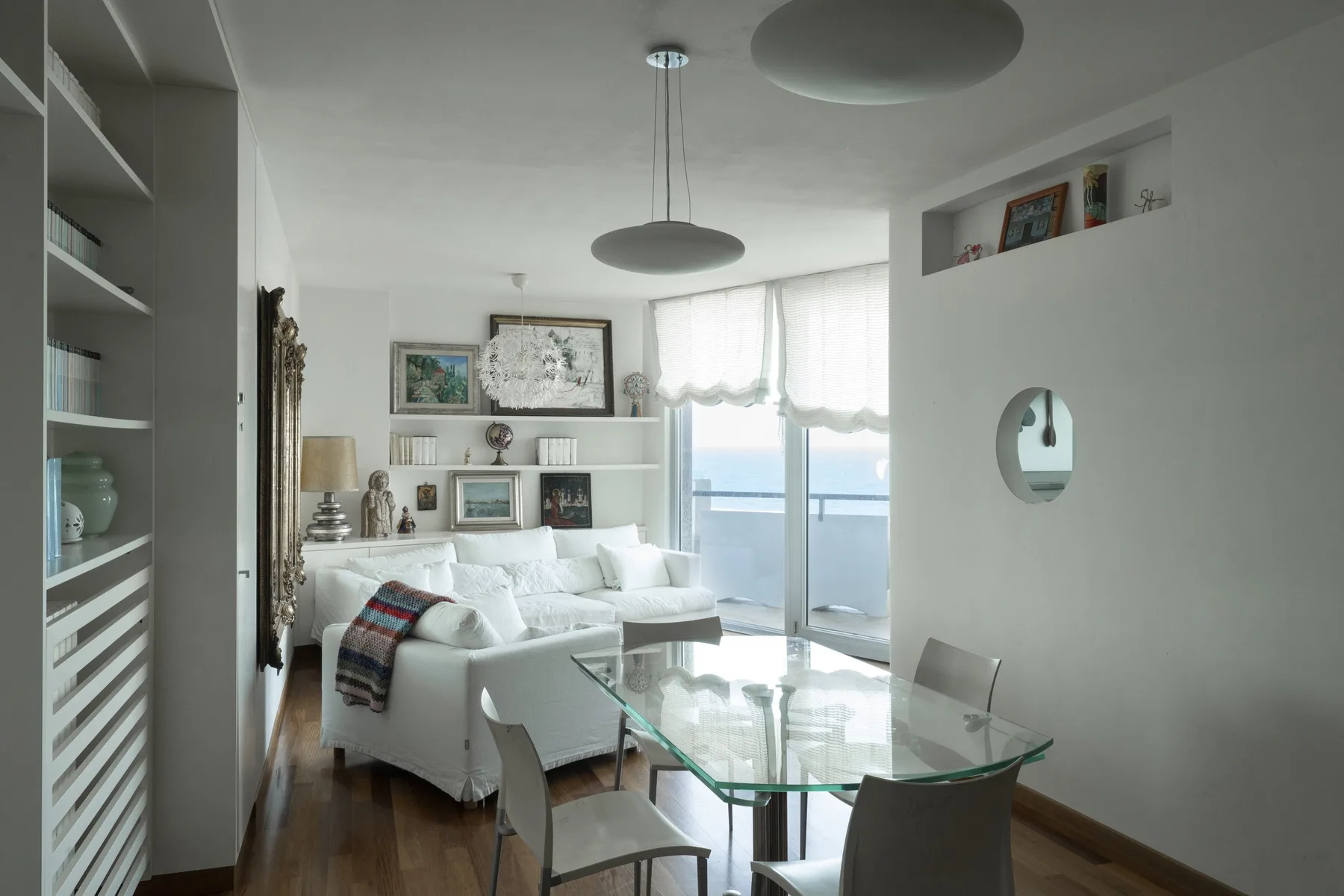 Una sala de estar luminosa con asientos, una mesa de vidrio y ventanas grandes.