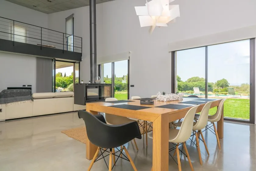 A modern open-plan living and dining area with a wooden table beside large windows.