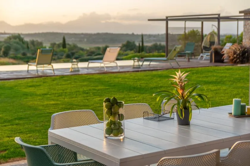 An outdoor dining area overlooks a lawn, pool, and distant hills.