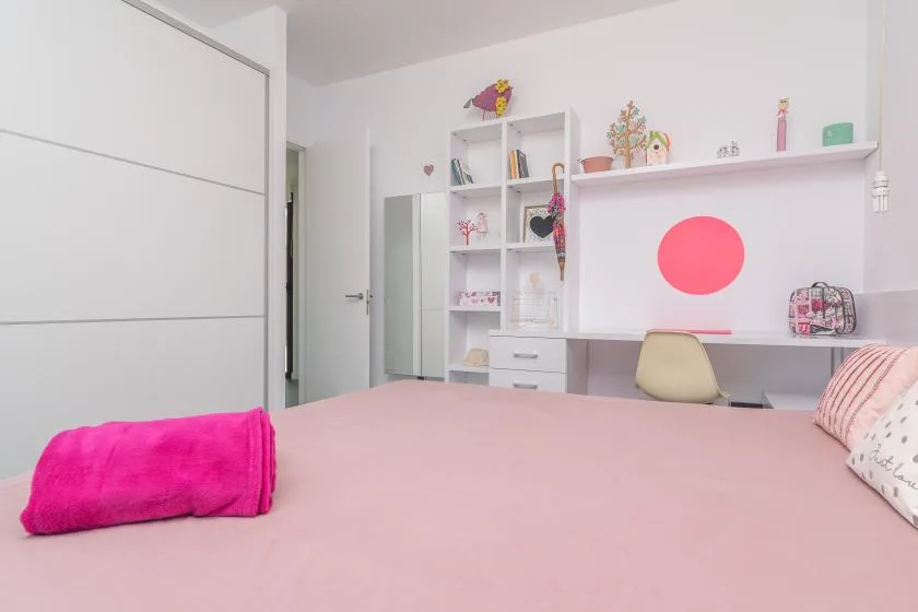 A pink bedroom with a bed, desk, and shelves along the wall.