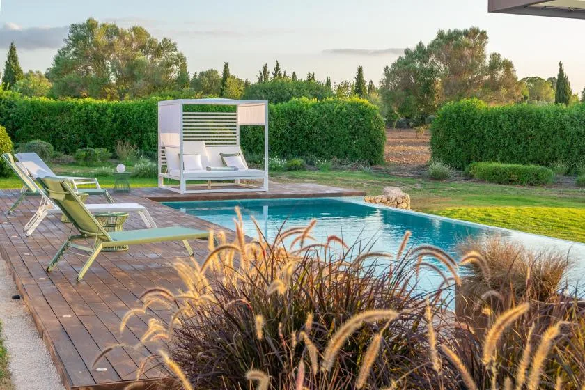 An outdoor swimming pool sits beside a wooden deck and garden.