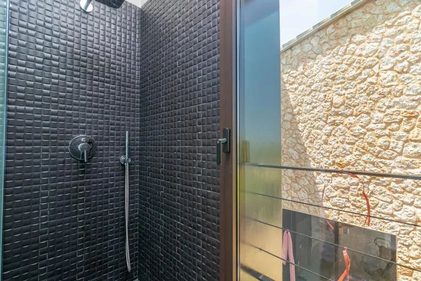An outdoor shower with dark tiled walls beside a glass door.