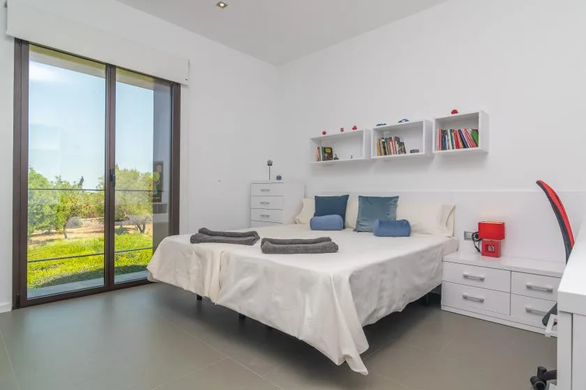 A bright bedroom with a bed, bedside drawers, and large glass doors overlooking greenery.