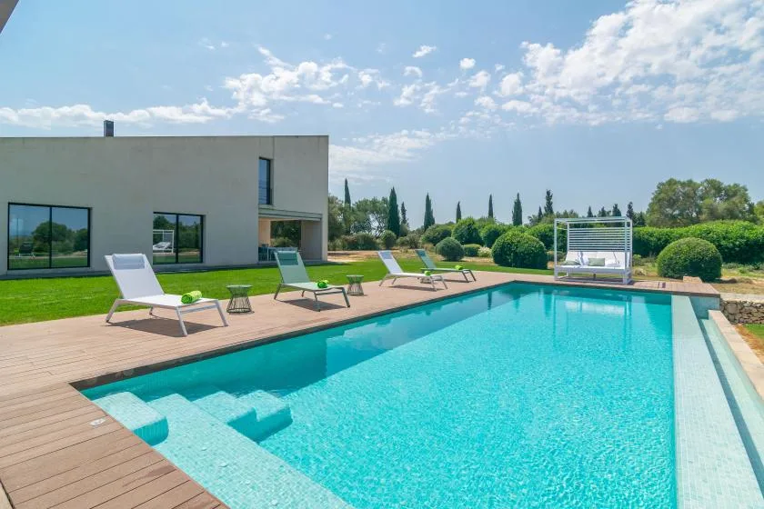 A swimming pool beside a modern house, with lounge seating on the deck.