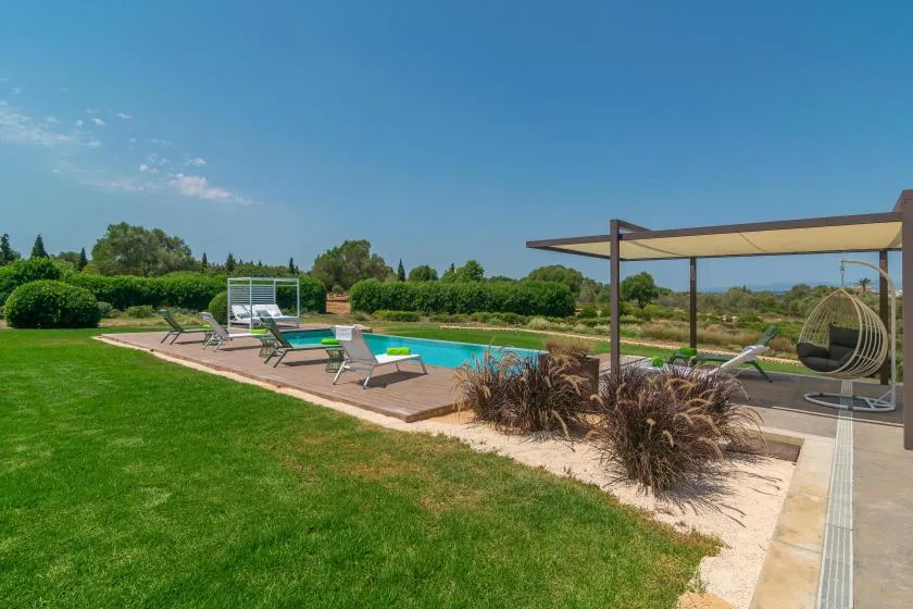 An outdoor swimming pool with loungers beside a grassy lawn.
