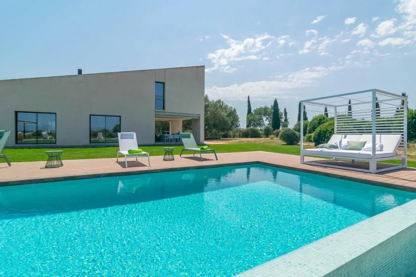 A swimming pool beside a modern building, with loungers arranged on the patio.