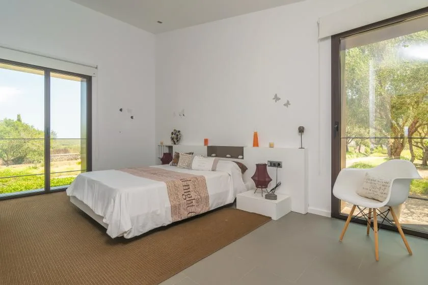 A bright bedroom with a neatly made bed and large windows overlooking greenery.