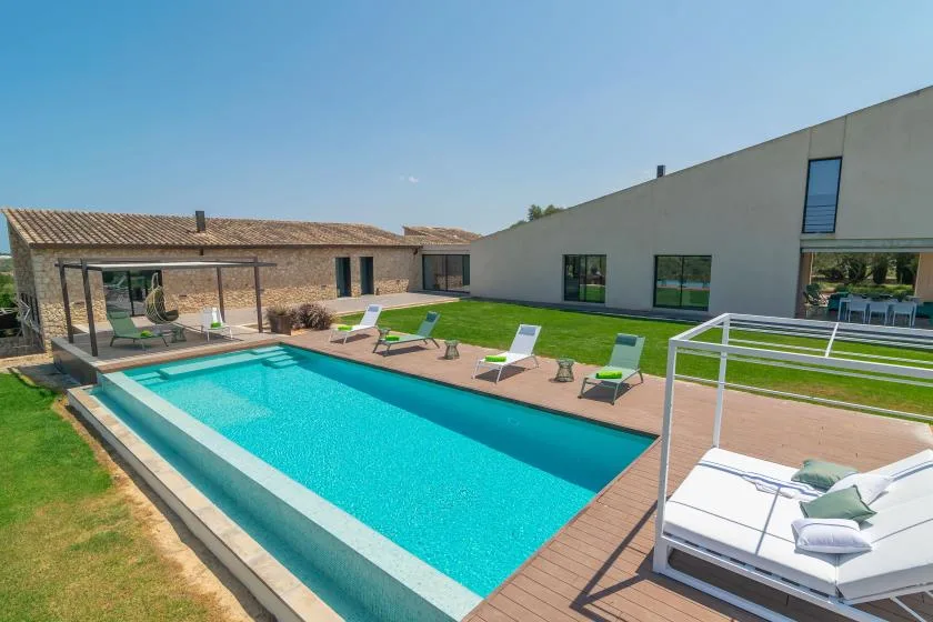 An outdoor swimming pool beside a modern building, with lounge chairs on the patio.