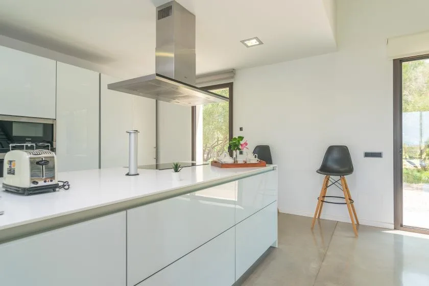 A bright modern kitchen with a long white island and stainless-steel range hood.