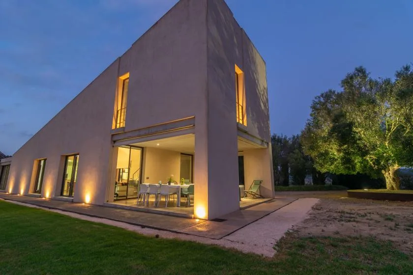 A modern house at dusk, with warm lights glowing through its windows.