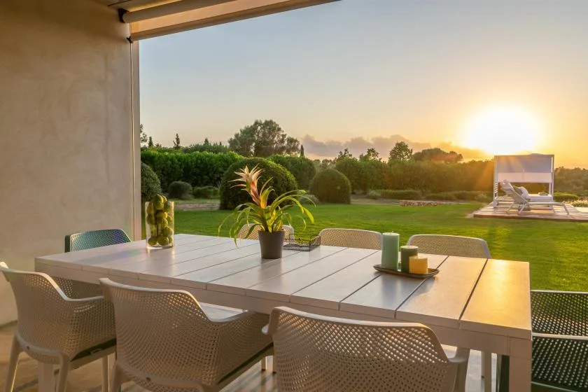 A patio dining area overlooks a lawn and garden at sunset.