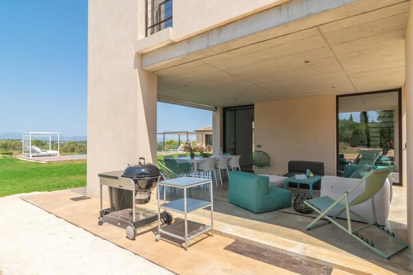 A covered patio with outdoor seating and a barbecue overlooks a lawn.