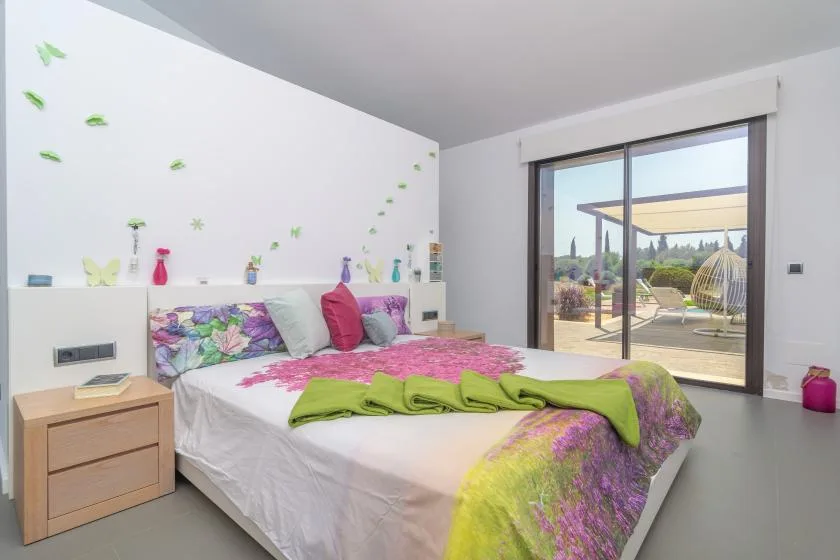 A bright bedroom with colorful floral bedding and a large glass door.