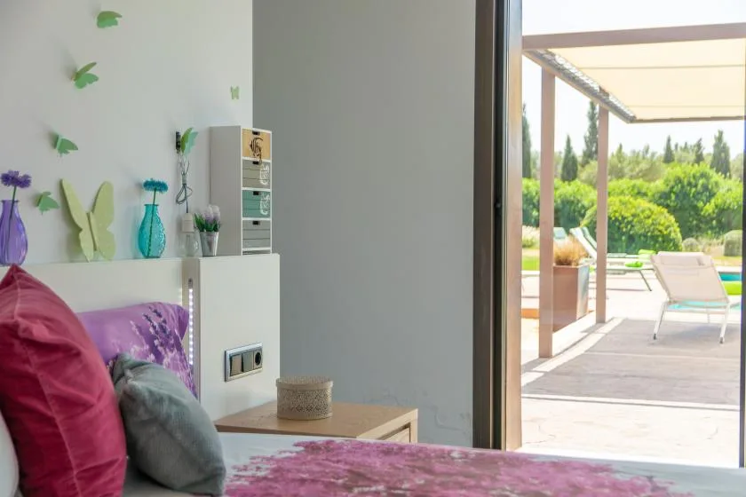 A bedroom opens onto a sunny patio with outdoor seating and greenery.