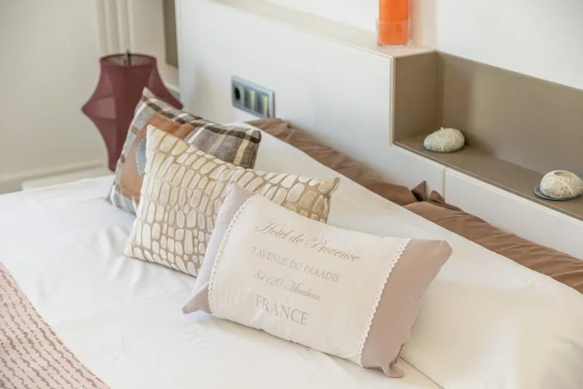 A neatly made bed with patterned pillows sits beside a wall shelf.
