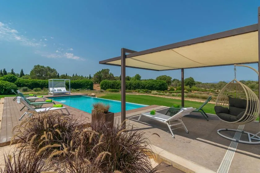 An outdoor swimming pool sits beside lounge seating beneath a shade canopy.
