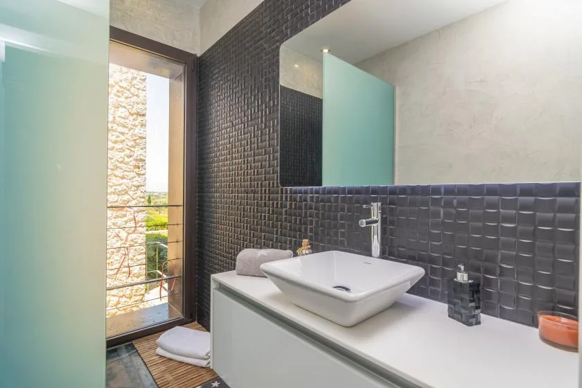 A bathroom vanity with a white vessel sink, dark tiled wall, and mirror.