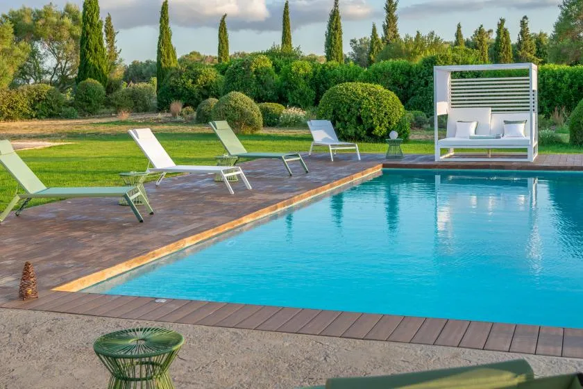 An outdoor swimming pool is bordered by a wooden deck and lounge seating.