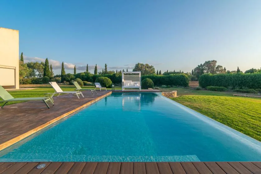 An outdoor swimming pool beside a lawn, with lounge chairs along the deck.