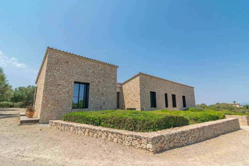 A low stone building stands beside a landscaped hedge under a clear blue sky.