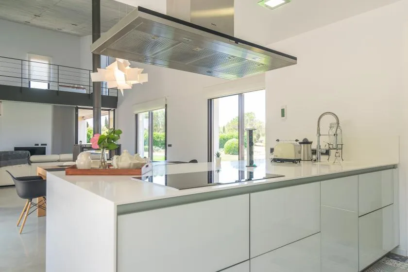 A modern kitchen with a large island and wide windows overlooking greenery.