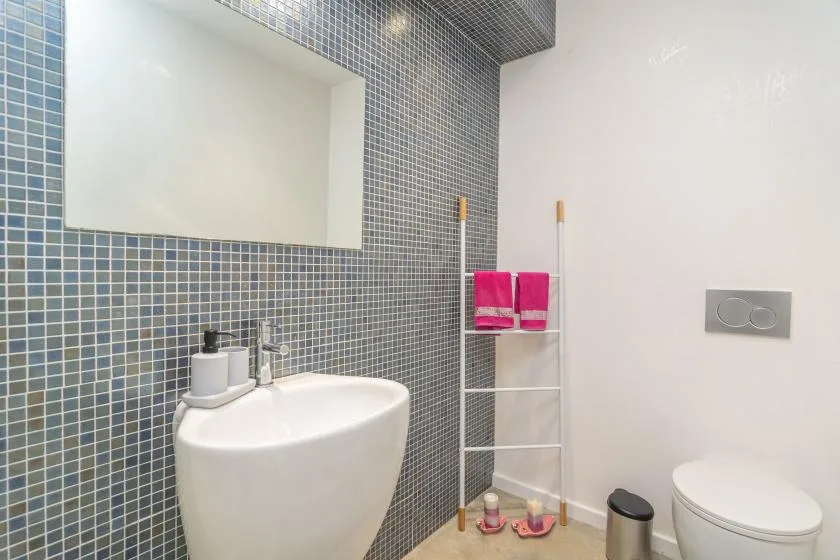 A tiled bathroom with a sink, toilet, and ladder-style towel rack.