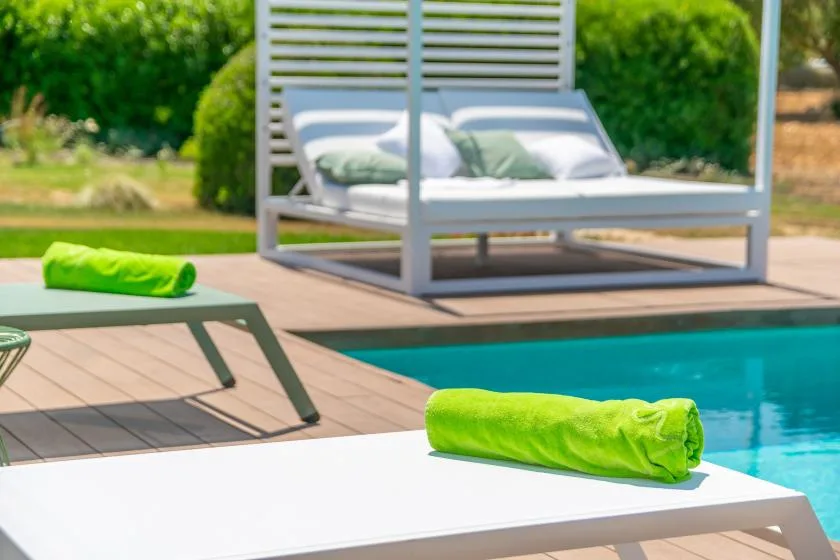 A poolside patio with a lounge bed and bright green towels.