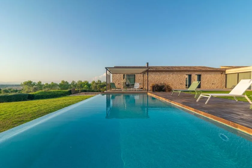 A swimming pool beside a low building, with lounge seating on the deck.