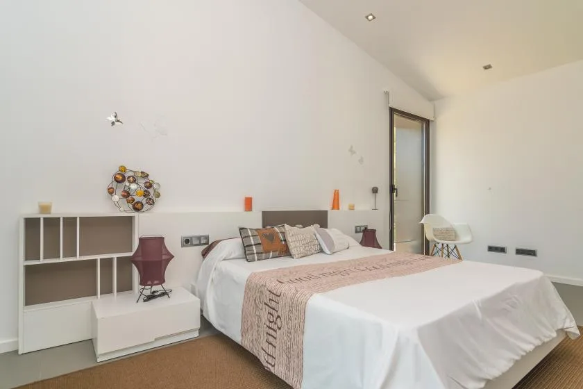 A bright bedroom features a bed with patterned pillows and a light-colored bedspread.