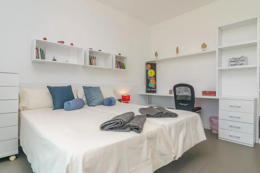A bedroom with a white bed, blue pillows, and built-in shelving.