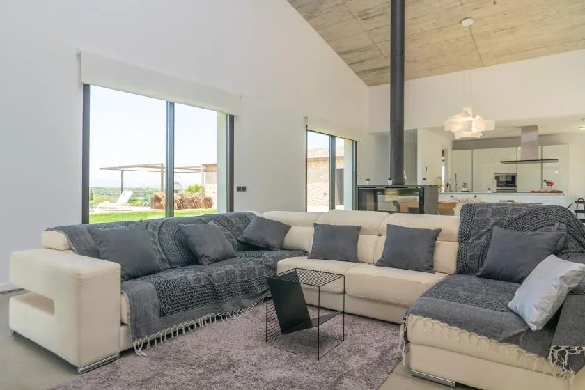 A bright living room has sectional seating facing a glass-fronted fireplace and open kitchen.