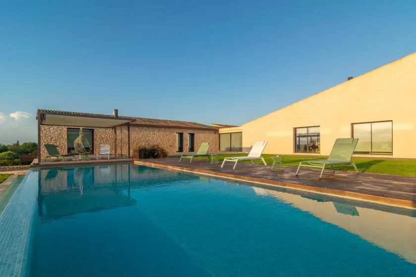 An outdoor swimming pool beside a modern building and deck seating.