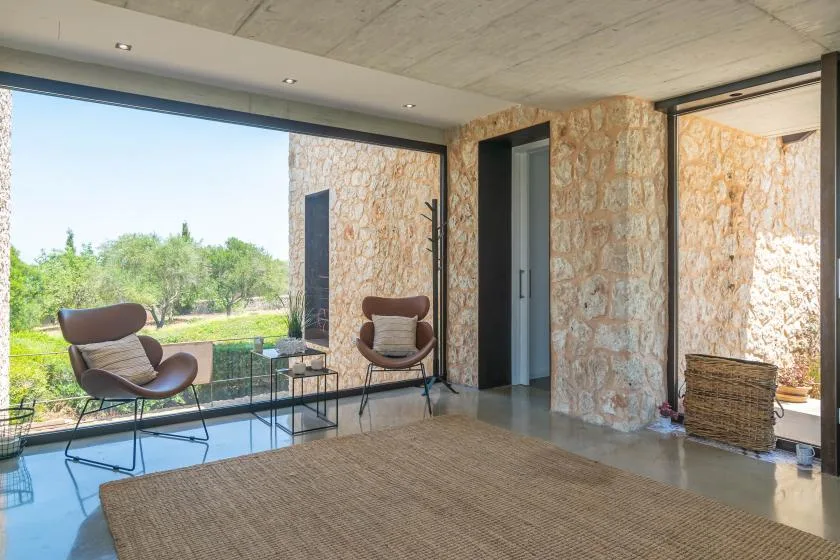 A bright stone-walled living area opens onto a garden through large glass windows.