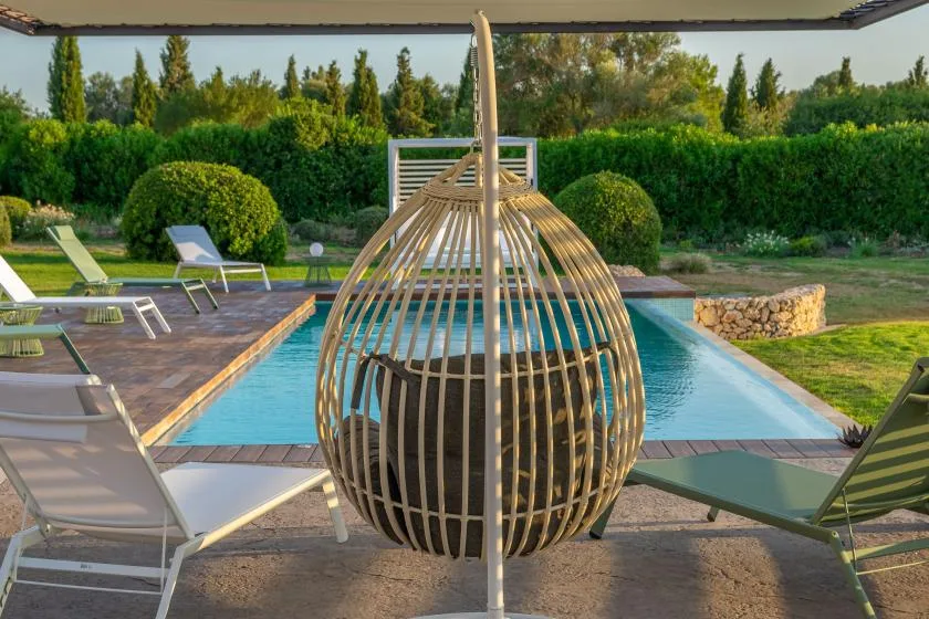 A swimming pool bordered by lounge seating and a hanging chair.
