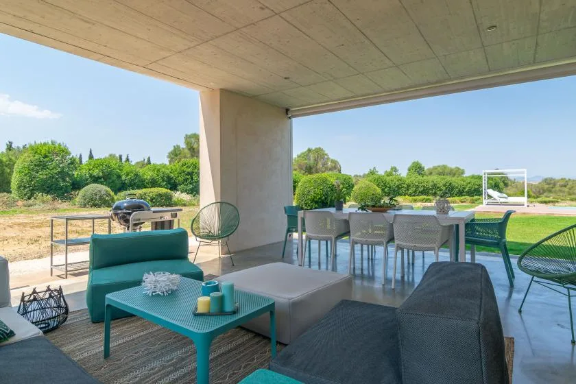 A covered outdoor patio with seating and a dining table overlooks a green garden.