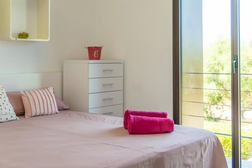 A bedroom with a bed, pillows, and a sliding glass door.